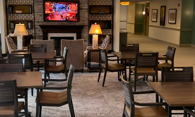 Senior living community common area with chairs, tables and fire place.